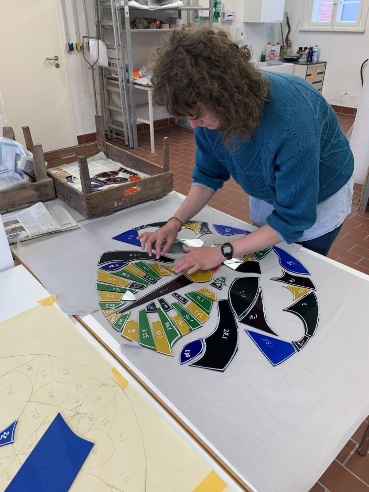 Zu sehen ist, die Künstlerin, wie sie ein Fensterbild gestaltet. Das Bild ist rund und noch nicht fertig