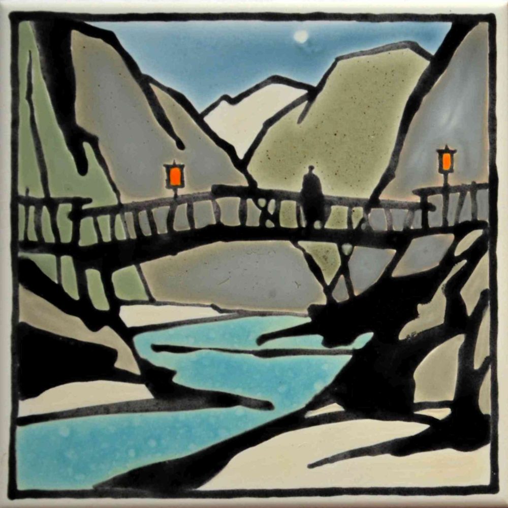 Auf der Bildfliese ist eine Berglandschaft zu sehen, durch die sich ein Fluss schlängelt. Zudem sieht man eine Brücke über diesem Fluss, auf der ein Mann steht.