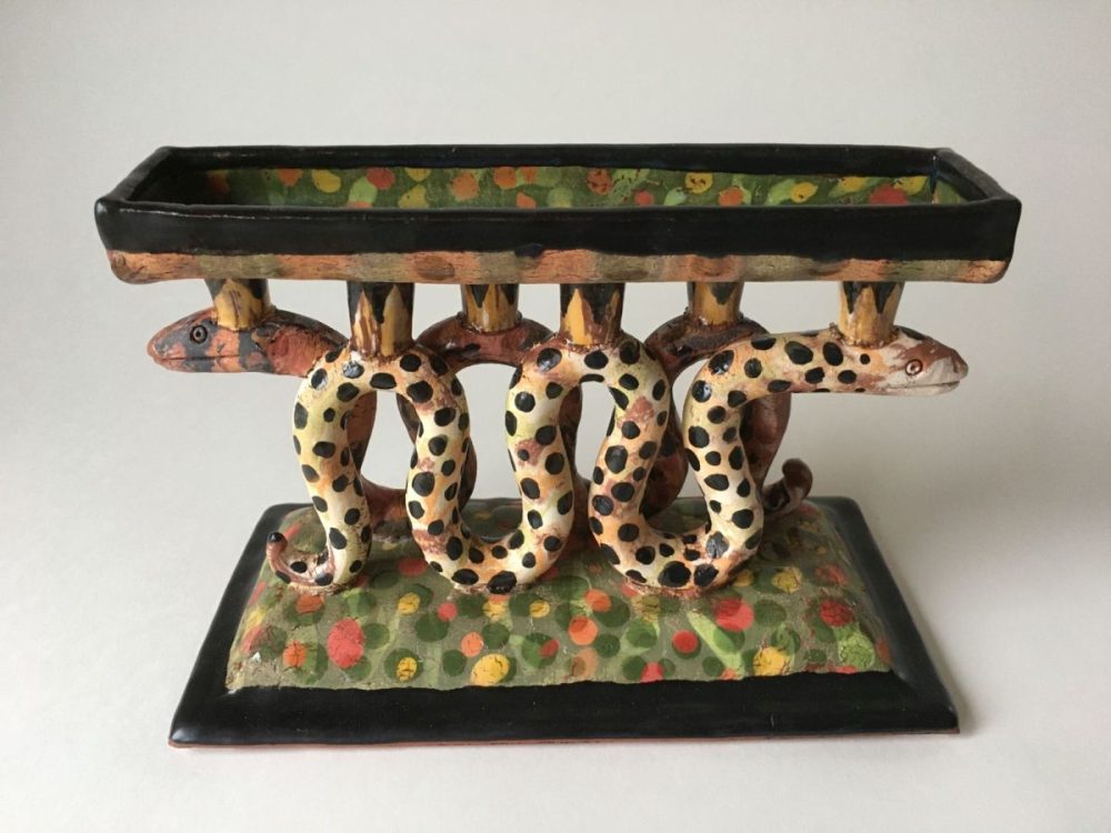 Zwei ineinander verwundene Schlangen mit gepunketen Schuppen. Auf ihnen ist eine Platte