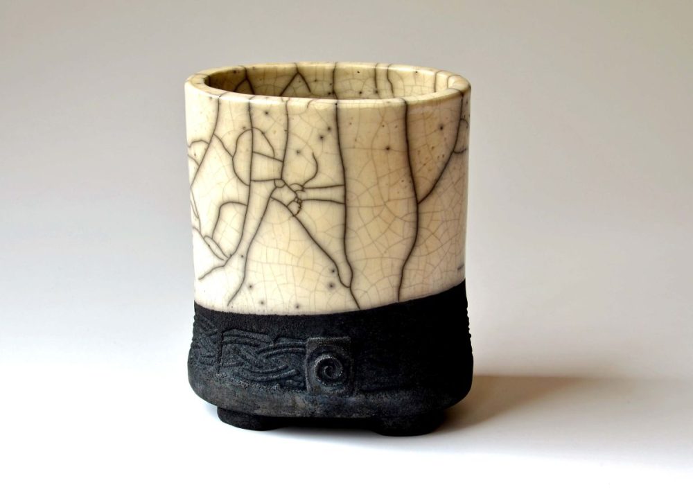 Ein Gefäß mit dunklem unteren Teil. Zwei Drittel des Gefäßes haben helle Farbe und sind mit dunklen Rissen verziert.