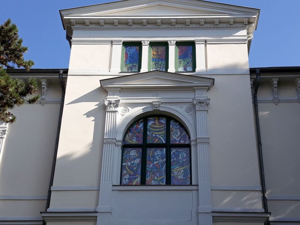 Zu sehen ist die Fesnterfront an der Nordseite des Apoldaer Kunsthauses. 3 kleine Fesnter unter demDach und ein größeres Fesnter mit Bogen wurden mit farbigen Gemälden ausgestattet.