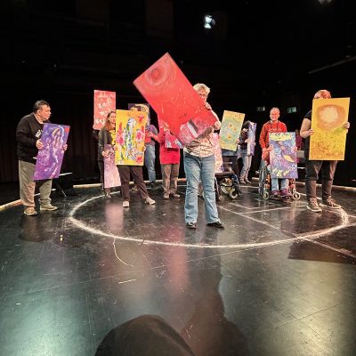 Blick auf die Probebühne im Theaterhaus Jena zur Aufführung des Inklusionsprojektes, viele Menschen mit bunten Bildern