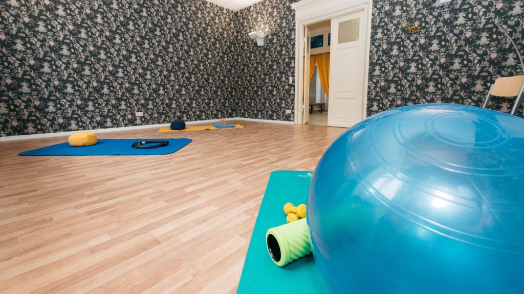 Sportraum der vhs Jena in der Schillerstraße. Im Vordergrund ein großer, blauer Gymnastikball und eine Matte. Im Hintergrund eine Wand mit dunklem Muster.