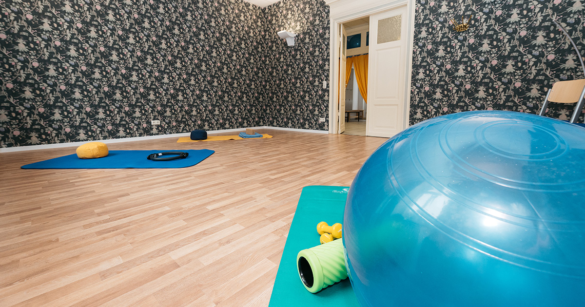 Sportraum der vhs Jena in der Schillerstraße. Im Vordergrund ein großer, blauer Gymnastikball und eine Matte. Im Hintergrund eine Wand mit dunklem Muster.