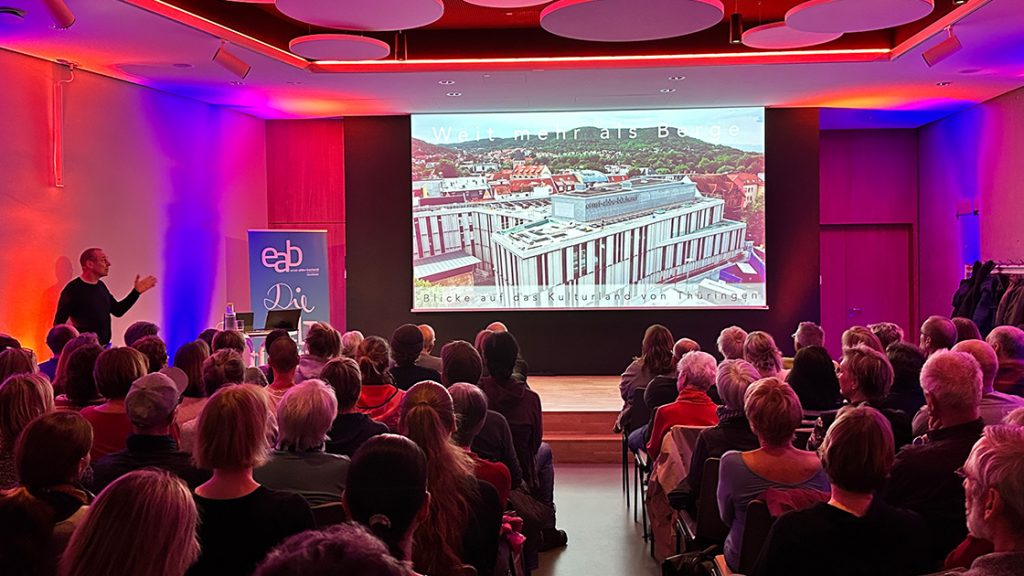 Blick auf eine Bühne mit einer Präsentation und Publikum