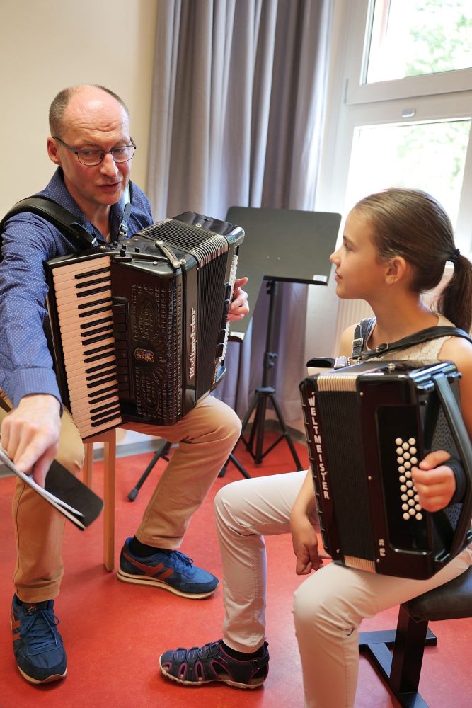 Akkordeonunterricht mit Stephan Bahr, ein kleines Mädchen hört aufmerksam zu