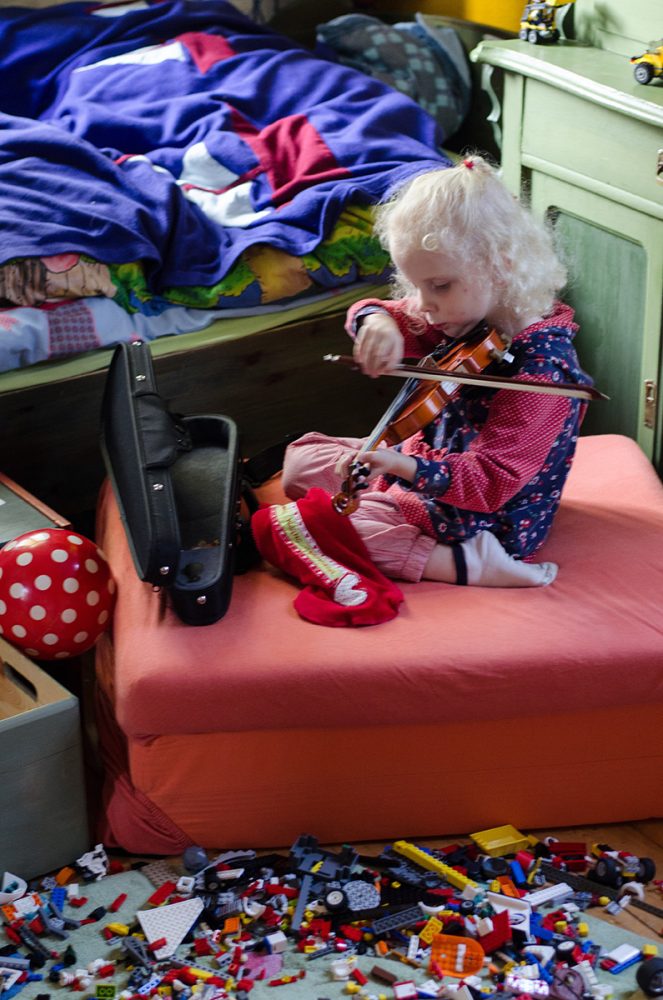 Elsa-Johanna Staemmler sitzt als Kind auf einem Kissen und spielt auf einer ganz kleinen Geige