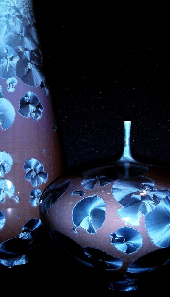 Detailaufnahme einer verzierten Keramikvase mit blauen kristallartigen Mustern vor schwarzem Hintergrund.