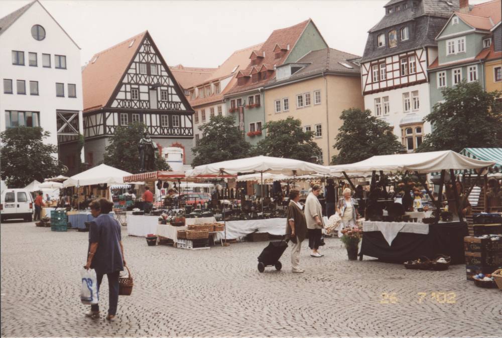 Belebter Wochenmarkt auf einem Kopfsteinpflasterplatz mit historischen Fachwerkhäusern im Hintergrund und mehreren Marktständen.