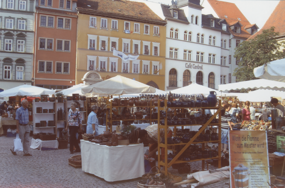 Töpfermarkt auf Stadtplatz, viele Keramikstände vor bunten Altbaufassaden, Menschen bummeln zwischen den Buden.