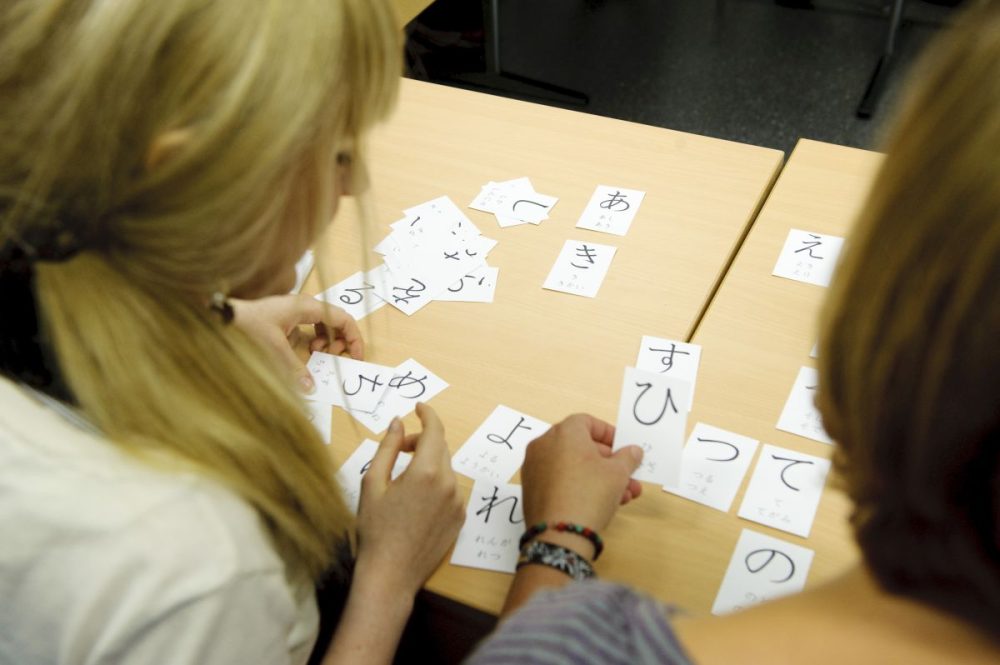 Ein Japanisch-Kurs in der vhs Jena, Schriftzeichen liegen wir Karten auf einem Tisch, 2 Schüler:innen beschäftigen sich damit