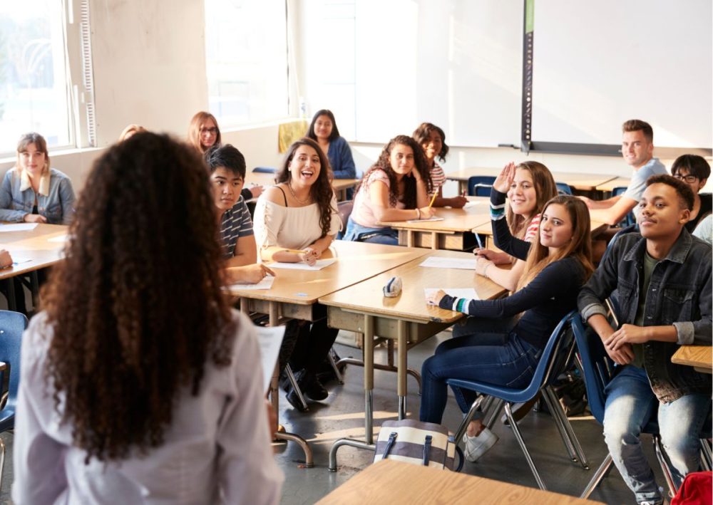 Schüler:innen in einem voellen Klassenzimmer, in der Mitte von hinten die lehrende Person