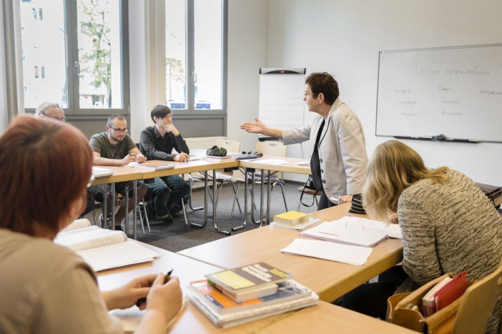 Blick in einen Unterrichtsraum der vhs Jena, ein Sprachkurs mit mehreren Teilnehmer:innen, die Lehrerin in der Mitte zeigt auf einen Schüler