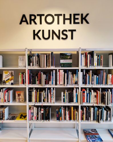 Bücherregal mit Kunstbüchern. Oben drüber hängt ein Schild mit der Aufschrift Artothek und Kunst