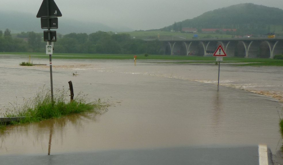 Man sieht eine Straße die in das Hochwasser führt. Im Hintergund ist die Autobahnbrücke der A4 bei Jena zu sehen.