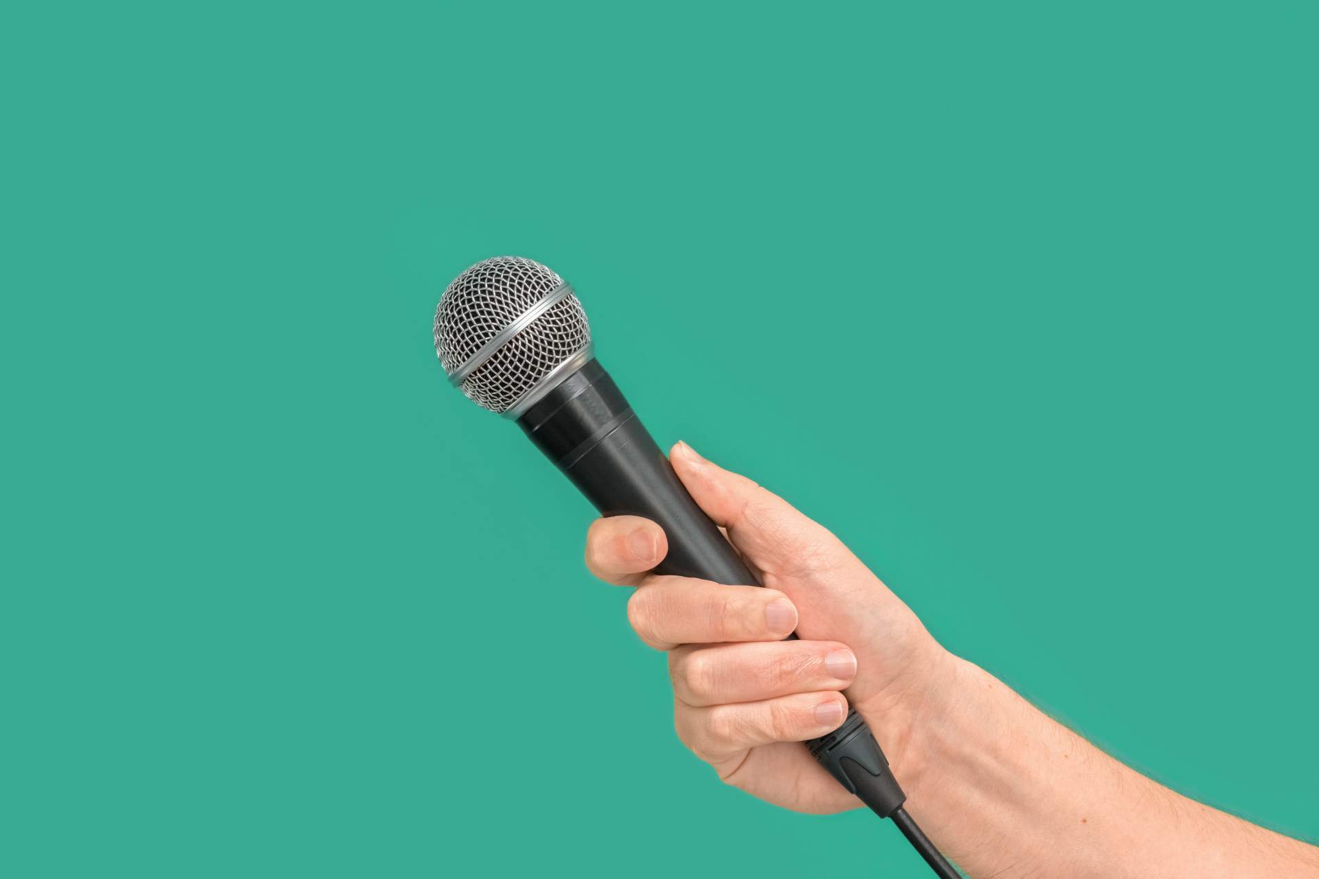 Hand hält Mikrofon vor grüner Wand.