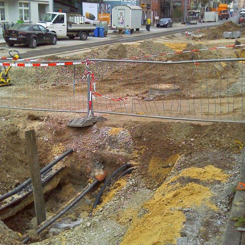 Tiefbauarbeiten / Straßenbau in Jena. Man sieht eine aufgerissene Straße mit verschiedenen Erdstoffen udn Schotter. Darin befindet sich eine Versorgungsleitung. Die Baustelle ist mit Gittern und Flatterband abgesichert.- Symbolfoto © KSJ